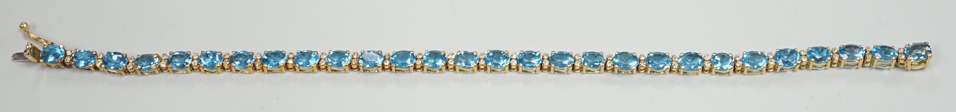 A modern 750 yellow metal and blue topaz set line bracelet, with diamond chip spacers, 17.75cm